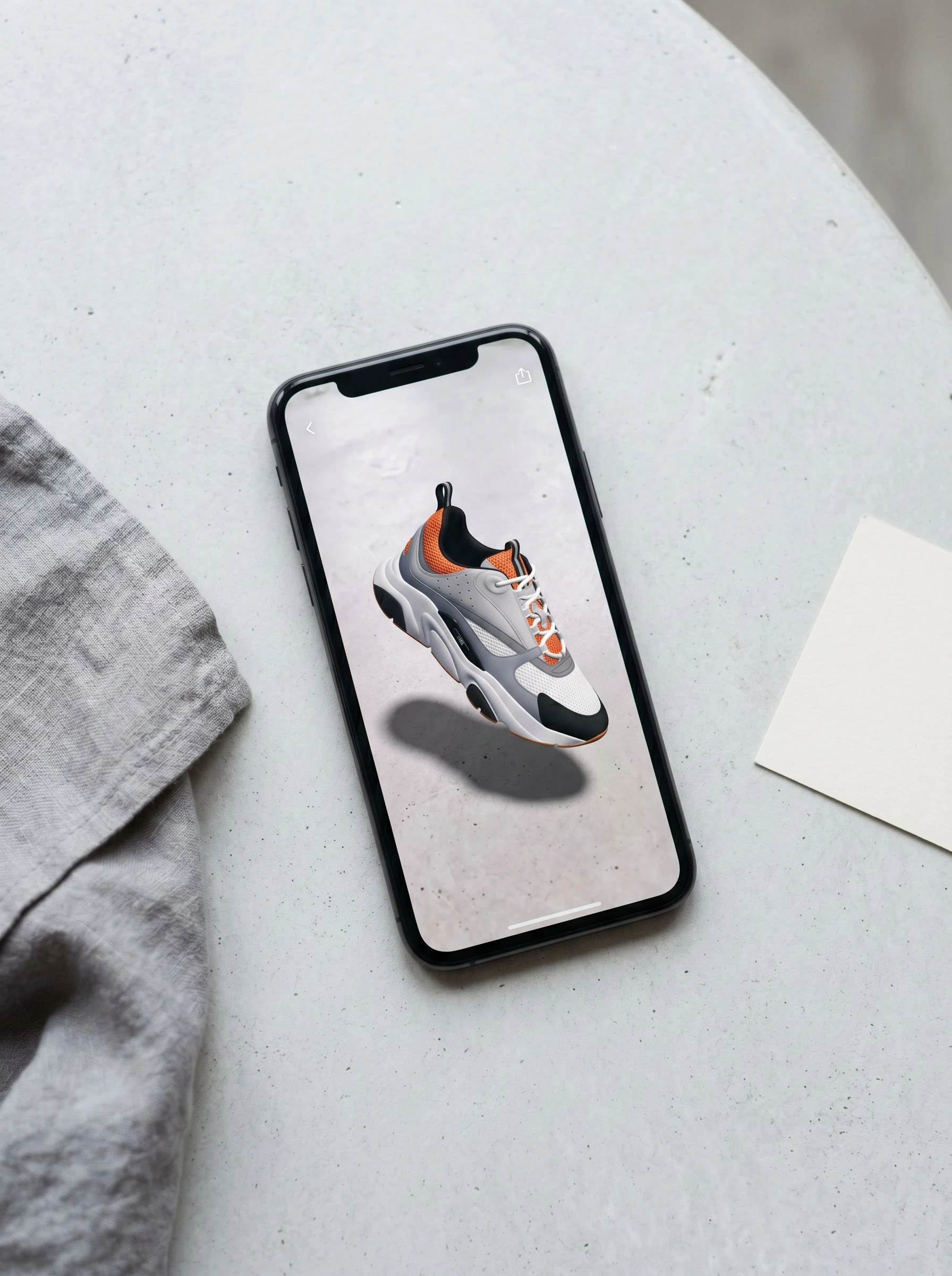 Phone showing a product try-on AR experience with trainers overlaid on a tabletop